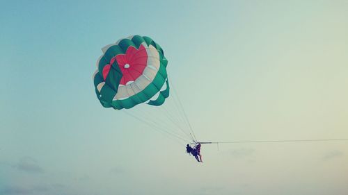 Low angle view of people parasailing against sky