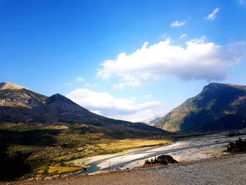 Scenic view of road by mountains against blue sky