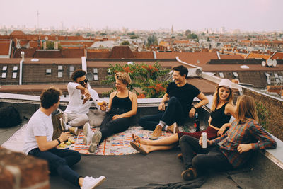 Happy friends enjoying beer while sitting at terrace during rooftop party in city