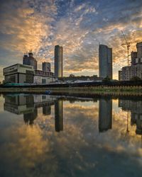 Reflection of buildings in city against sky during sunset