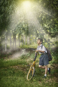 Smiling schoolboy standing with bicycle at park