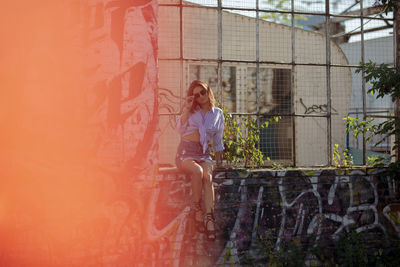 Young woman sitting on window sill amidst graffiti wall