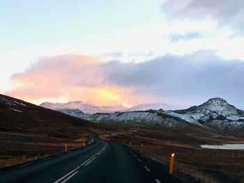 Empty road by snowcapped mountains against sky during sunset