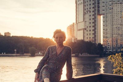 Young woman looking away in city against sky during sunset