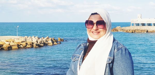 Portrait of smiling young woman by sea against sky