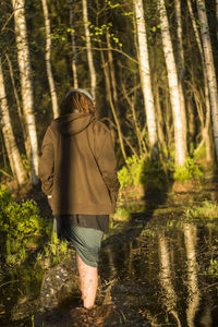 Rear view of woman walking in lake against trees at forest