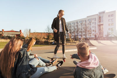 Friends looking at teenage girl skateboarding at park in city