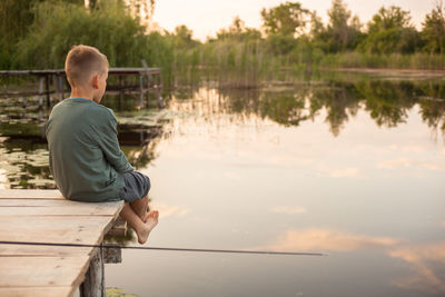Rear view of boy sitting on pier over lake