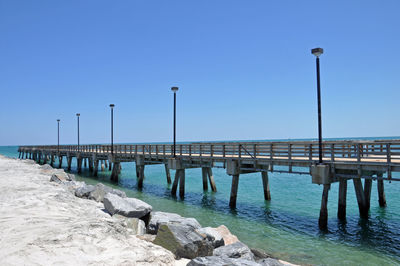 Pier on sea against clear blue sky