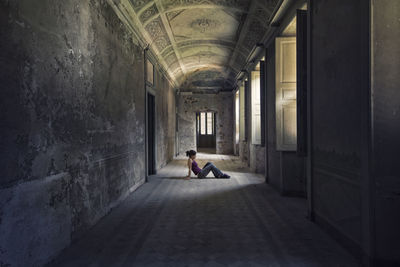 Woman sitting at corridor of abandoned building