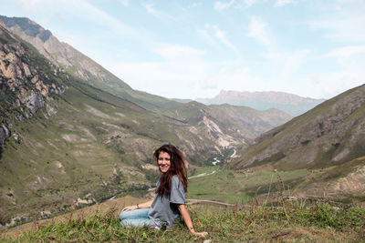 Portrait of young woman sitting against mountain range