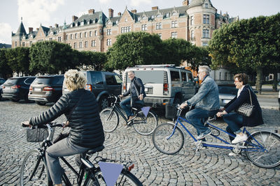 Senior male and female friends riding bicycles on street in city