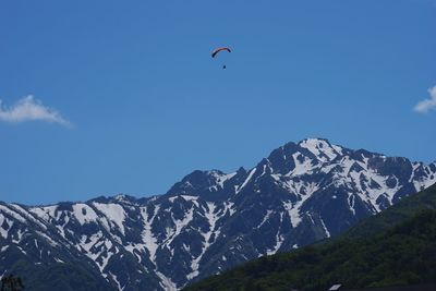 Person paragliding over snowcapped mountain against sky