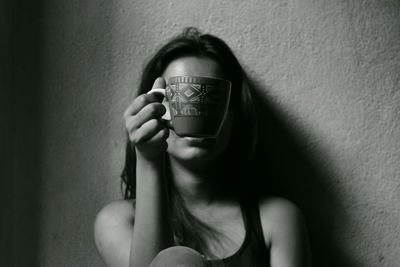 Woman with face covered by coffee cup against wall