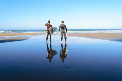 Friends standing on beach against clear blue sky