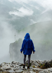 Girl with rainproof coat standing on a rock in foggy weather