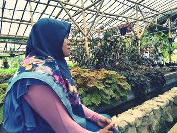 Side view of young woman standing in greenhouse