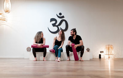 Young man and women with mats speaking with each other while sitting in white block in spacious studio during yoga training