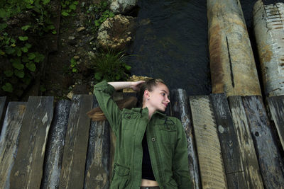 High angle view of smiling woman lying on footbridge over river at forest