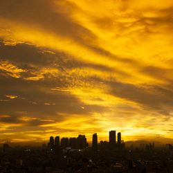 Silhouette buildings against dramatic sky during sunset