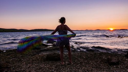 Rear view of woman at beach against sky during sunset