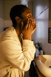 Young woman applying moisturizer on face at home