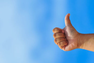 Low angle view of hand showing thumbs up sign against clear blue sky