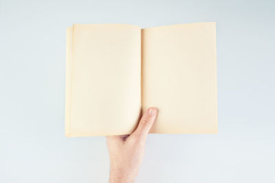 Close-up of hand holding book against white background