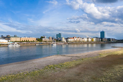 View of buildings by river against cloudy sky