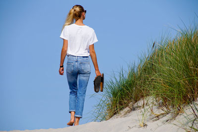 Rear view of woman walking at beach against clear blue sky