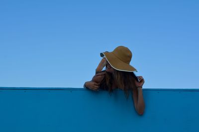 Low angle view of young woman on wall against clear blue sky