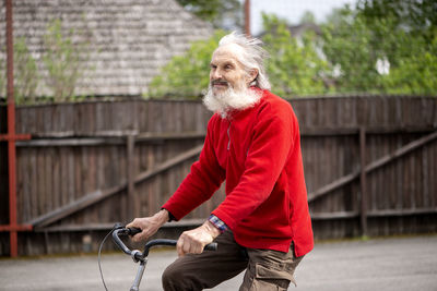 Sad old bearded man riding a bicycle wearing a red sweater, hair fluttering in the wind