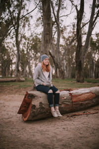 Full length of teenage girl sitting on tree in forest