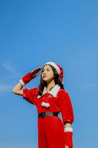 Low angle view of young woman looking away against blue sky