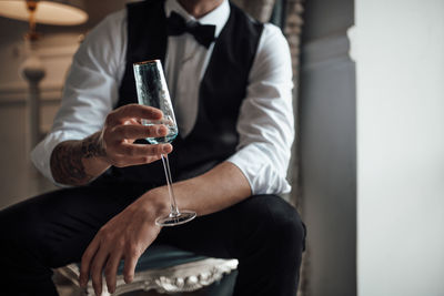 Midsection of man holding wine while sitting on table