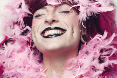 Close-up of woman with make-up smiling amidst pink feathers