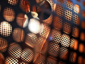 Close-up of illuminated light bulb amidst metal grids