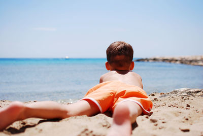 Side view of boy in shorts lying at beach against sky