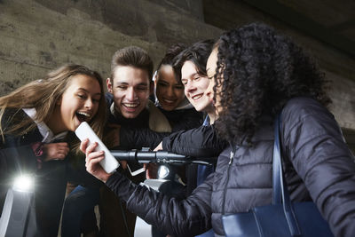 Teenage girl showing mobile phone to happy male and female friends