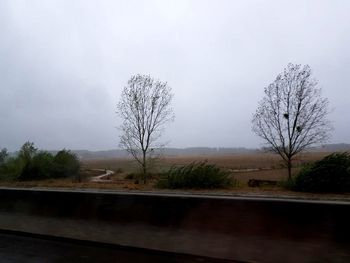 Bare trees on landscape against sky during rainy season