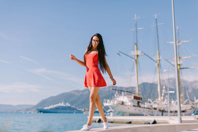 Full length portrait of young woman on promenade by sea against sky