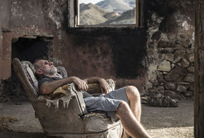 Adult man sitting on an old sofa of an abandoned house