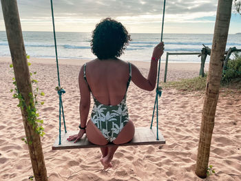 Rear view of woman sitting on swing at beach