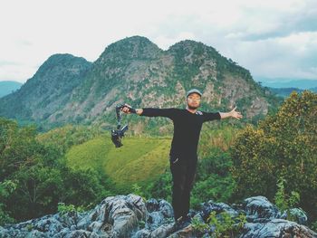 Young man standing on cliff against mountains