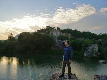 Man standing on rock at lakeshore against sky