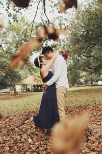 Side view of man and woman holding autumn tree
