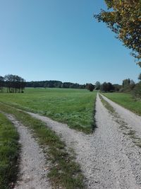 Road amidst field against clear sky