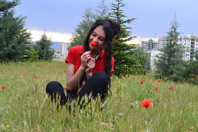 Young woman smelling flowers while sitting on land