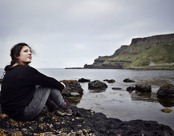 Young woman looking up while sitting on rock by sea