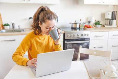 Young woman using laptop while sitting on table